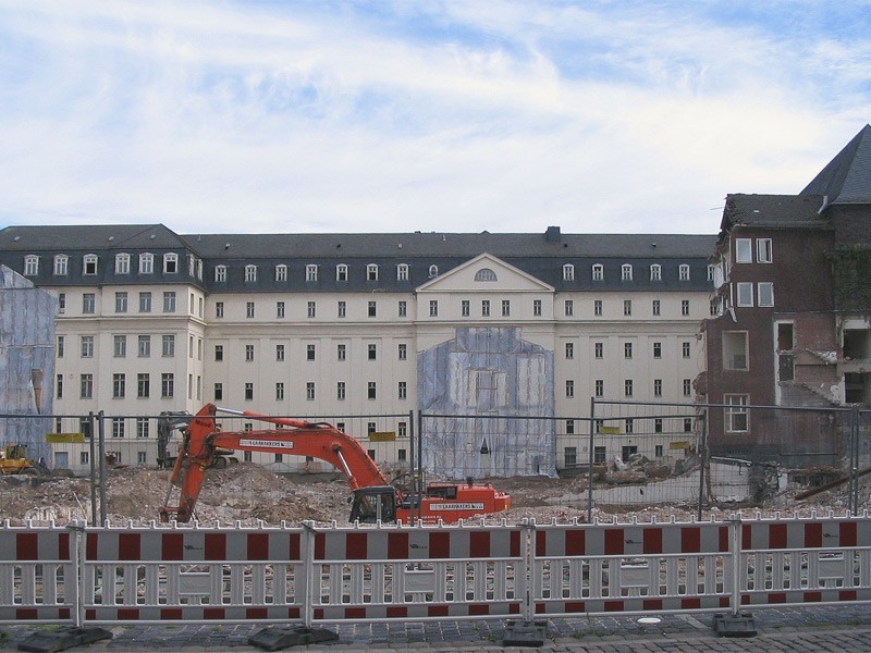 Construction site scene in front of a historic building complex in Düsseldorf with demolition work, excavator and cordoned-off construction area.