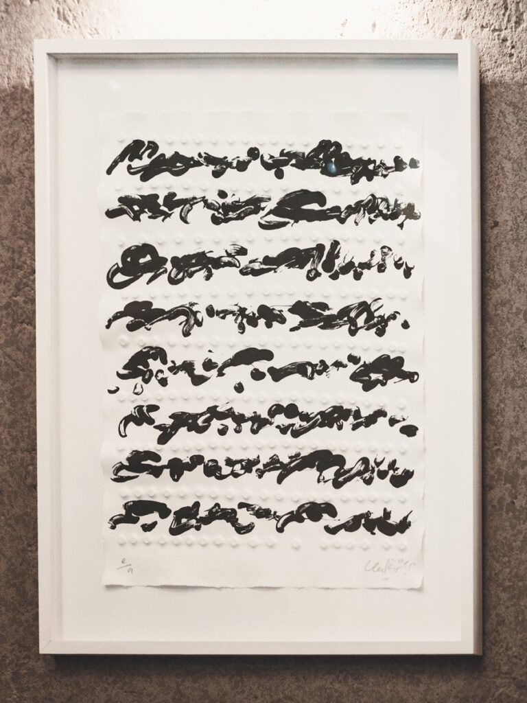 Gerahmtes abstraktes Kunstwerk im Hotel The Wellem Düsseldorf mit schwarzen Pinselstrukturen auf weißer reliefartiger Oberfläche.