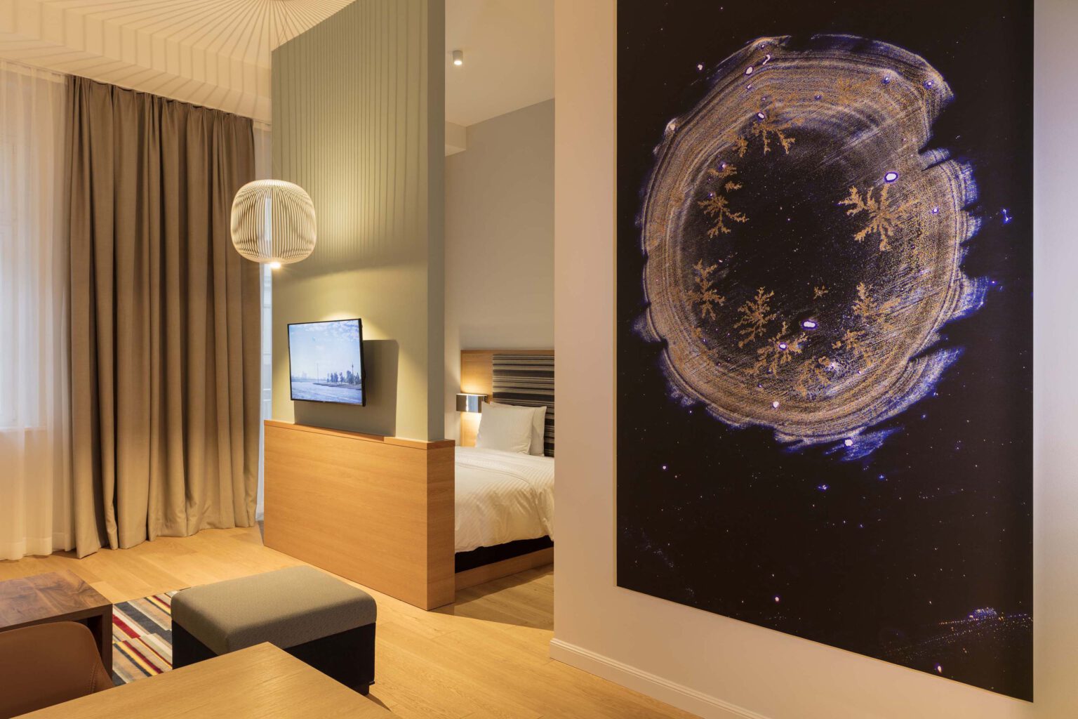 Bright studio suite with modern living and sleeping area, large abstract artwork, elegant wooden interior and cozy lighting at Hotel The Wellem in Düsseldorf.