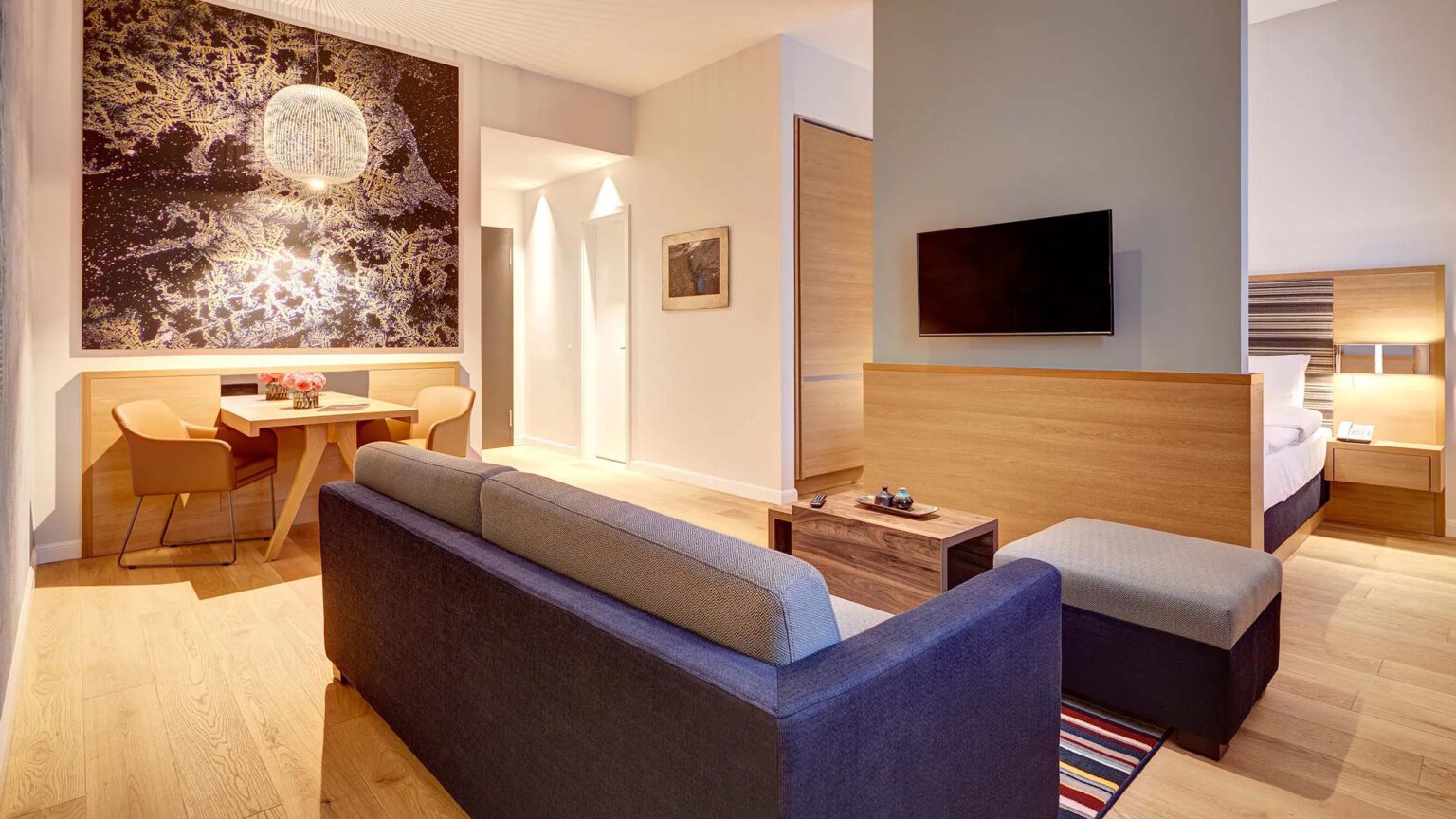 Modern studio suite with open-plan living and sleeping area, elegant wooden accents, large-scale artwork and stylish seating area at The Wellem Hotel in Düsseldorf.