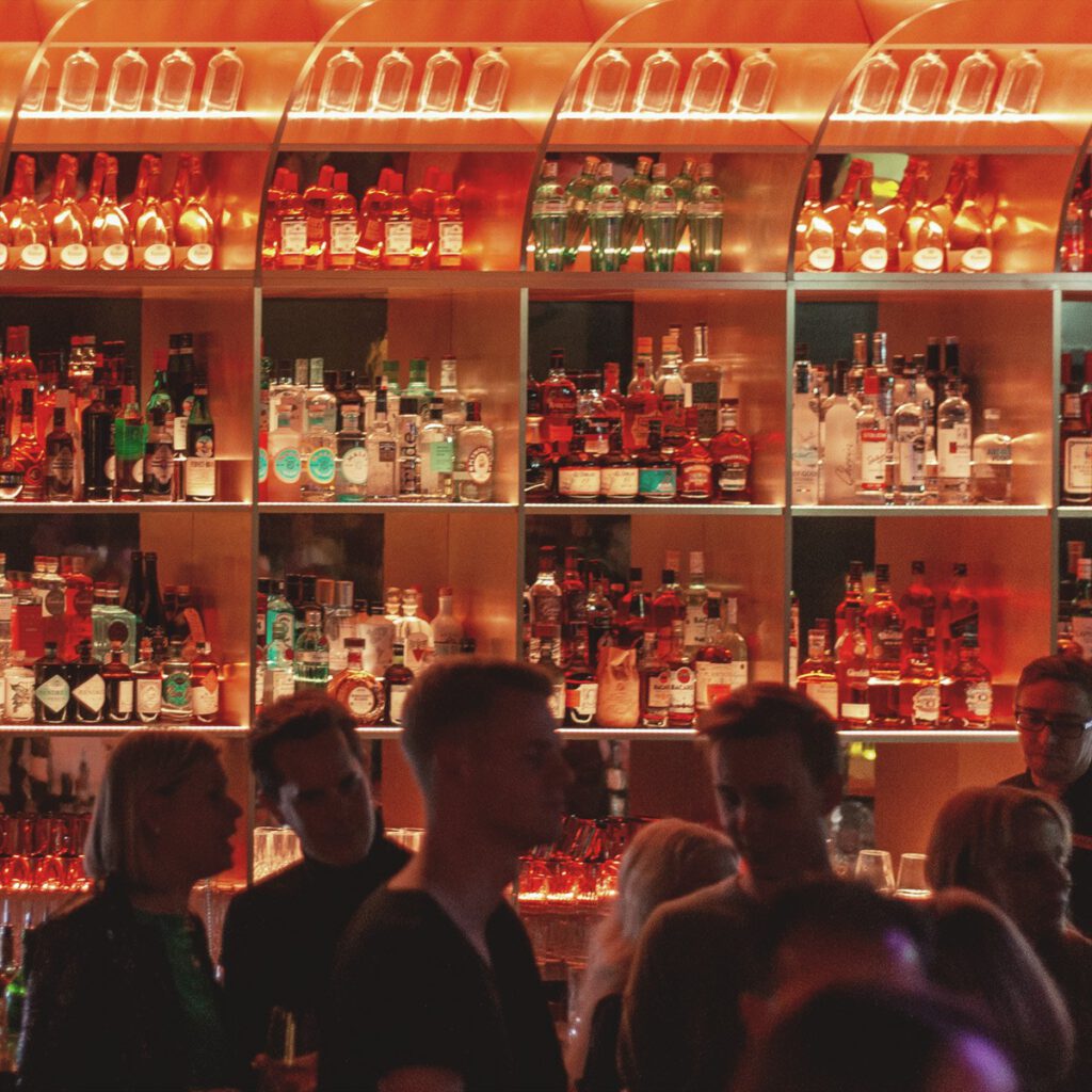 Stylish bar atmosphere with illuminated bottle wall and guests at Franks Club in the Andreas Quartier Düsseldorf, part of the exclusive nightlife experience at Hotel The Wellem.
