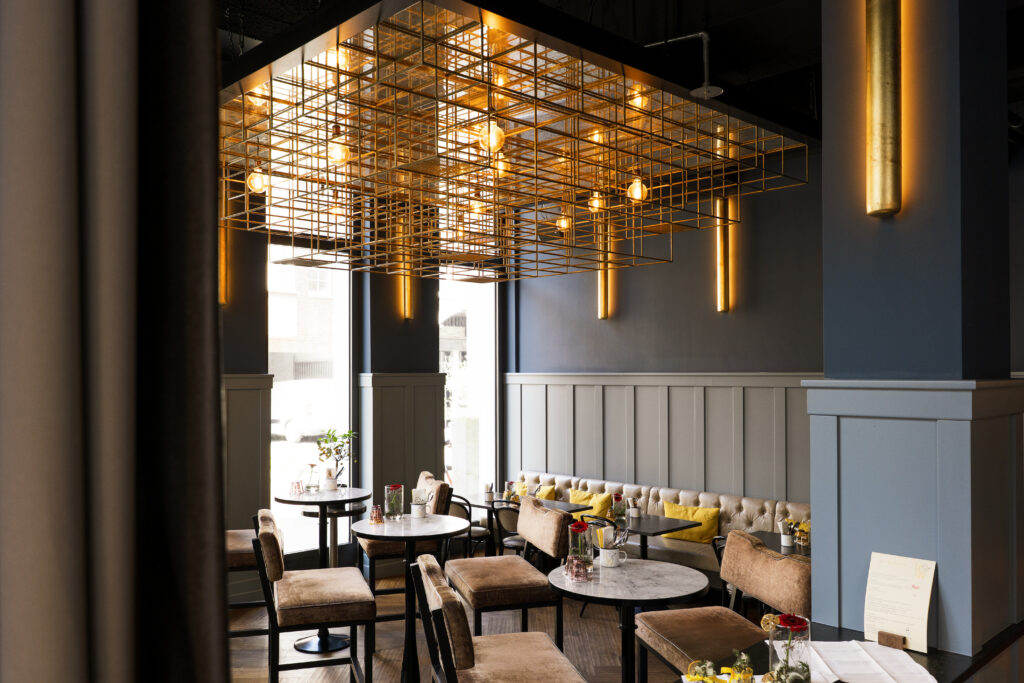 Modern interior of the restaurant Le Cou Cou in The Wellem Düsseldorf with golden grid ceiling installation, round marble tables and cozy seating areas.