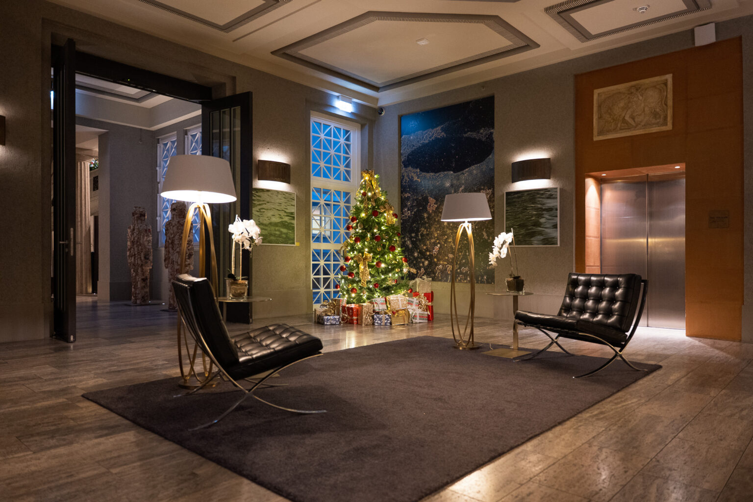 Weihnachtlich geschmückte Lobby im Hotel The Wellem Düsseldorf mit festlichem Christbaum, eleganten Lounge-Sesseln, Orchideen und kunstvoller Wandgestaltung in stimmungsvoller Beleuchtung.