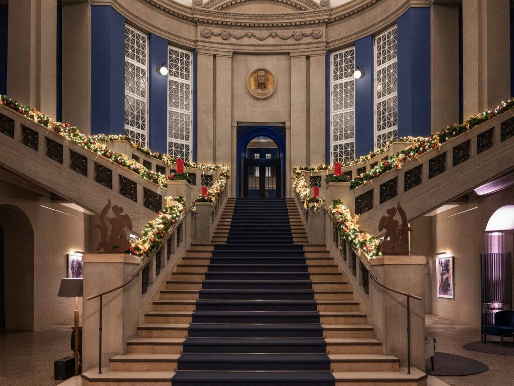Festively decorated historic staircase at Hotel The Wellem Düsseldorf with opulent Christmas lights, wreaths, red candles and elegantly illuminated classicist architecture.